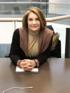 A woman sitting at a desk with hands clasped, smiling.